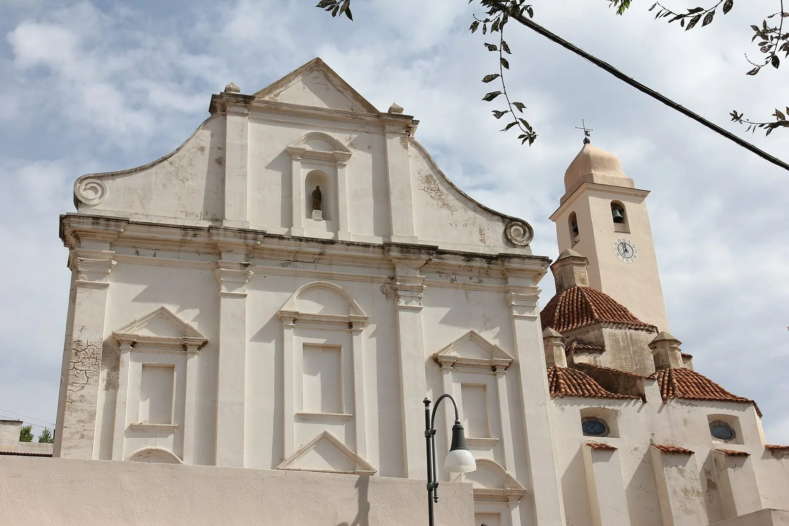 Facciata bianca della chiesa di San Giacomo Maggiore a Orosei con il campanile e le cupole rivestite di coppi