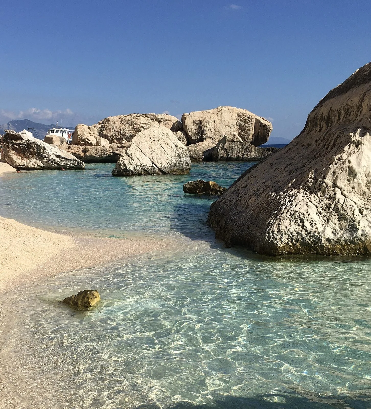 Acqua turchese e grandi massi calcarei bianchi a Cala Mariolu nel Golfo di Orosei, con una barca sullo sfondo
